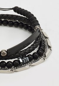 Pulsera negra de múltiples hebras con cuero texturizado, cuentas lisas y acentos metálicos. Incluye diseño trenzado y eslabones de cadena.