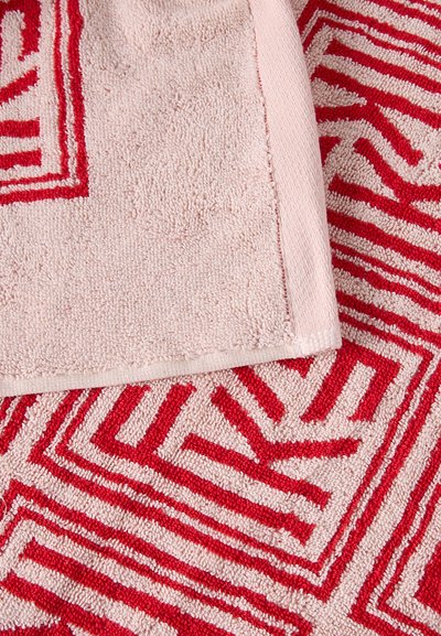 Μαλακή ροζ πετσέτα με κόκκινο γεωμετρικό μοτίβο που μοιάζει με λαβύρινθο, εμφανίζοντας και τις μπροστινές και τις διπλωμένες πίσω άκρες.