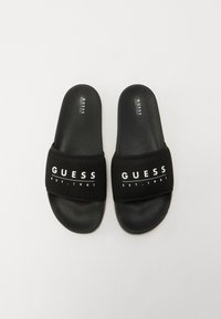 Fekete slides szandál textúrázott talppal és széles elasztikus pánttal, amelyen fehér betűkkel a "GUESS EST. 1981" felirat látható.