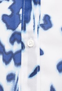 Πουκάμισο με κοντά μανίκια με αφηρημένο μοτίβο σε μπλε και λευκό, κατασκευασμένο από ελαφρύ ύφασμα, με κεντρικό κουμπί και αντίθετη ραφή.