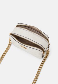 Sac en cuir blanc texturé avec deux compartiments zippés, une chaîne dorée et un motif en relief sur la surface.