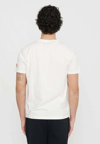 T-shirt en coton blanc avec un col rond classique, des manches courtes et une texture lisse. Présente un petit logo sur l'épaule gauche.