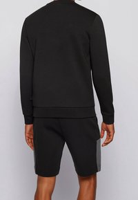 Felpa nera con collo e polsini a coste, abbinata a pantaloncini neri coordinati con pannelli laterali grigi. Tessuto morbido e strutturato.