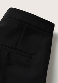 Gros plan sur un pantalon noir sur mesure montrant la ceinture et une seule poche arrière horizontale avec des coutures nettes.