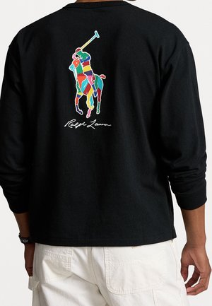 Czarna koszula z długim rękawem z kolorowym, abstrakcyjnym logo polo z graczem oraz podpisem "Ralph Lauren" na plecach, noszona z białymi spodniami.