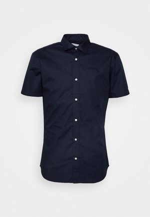 Camisa de manga corta en algodón azul marino. Cuenta con cierre frontal con botones, cuello estándar y dobladillo redondeado. Textura lisa con un sutil brillo.