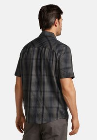 Chemise à manches courtes à carreaux gris foncé avec des motifs en quadrillage variés. Présente un empiècement au dos et une coupe décontractée. Texture de tissu légère.