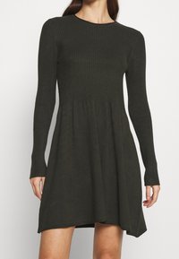 Abito a maglia verde scuro, corpino a costine con maniche lunghe, gonna svasata, texture morbida, scollatura tonda, orlo fino al ginocchio, design casual.