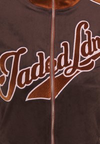 Veste en polaire marron zippée avec un grand texte en cursive vintage brodé sur la poitrine.