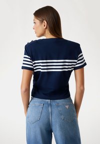 T-shirt tagliato blu navy con strisce orizzontali bianche, bottoni sulle spalle, abbinato a jeans leggeri a vita alta blu chiaro con tasche posteriori.
