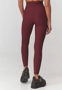 Bordowe legginsy wysokiej talii z prążkową teksturą, dopasowanym krojem i bezszwowym designem. Połączone z czarnymi, masywnymi Sneakersami.