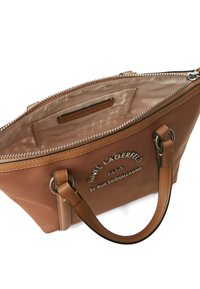 Brown handbag made of smooth material, featuring a zip closure, leather handles, and embossed branding on the front. Interior lined in satin.