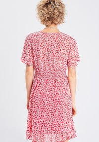 Robe courte à fleurs rouges en tissu léger, dotée de manches courtes évasées, d'une taille élastique et d'une silhouette fluide jusqu'aux genoux.