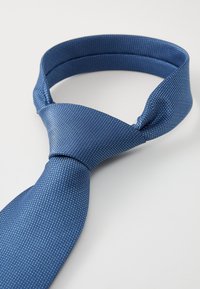 Blå slips med et teksturert mønster, med en smal ende og en bredere ende som danner en pen knute, alt på en hvit bakgrunn.