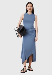 Abito senza maniche azzurro chiaro con un corsetto aderente, dettagli drappeggiati in vita e un orlo asimmetrico. Borsa nera e sandali con cinghie.