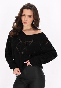 Maglione nero lavorato a maglia con un design oversize e scollato, caratterizzato da un motivo testurizzato e polsini a costine. Abbinato a pantaloni neri.