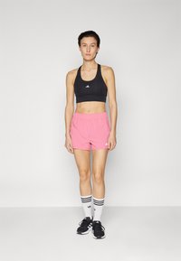 Čierny športový crop top, ružové šortky, biele športové ponožky s čiernymi pruhmi a čierne tenisky. Jednoduchý dizajn, elastický pás v šortkách.