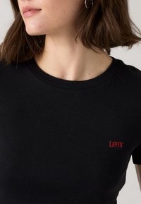 T-shirt noir à manches courtes côtelées avec un col rond et un logo Levi's rouge brodé sur la poitrine gauche. Texture en coton doux.