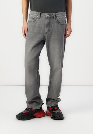 Jeans in denim grigio con vestibilità classica, caratterizzati da gamba dritta, design a cinque tasche e leggere sfumature. Indossati con sneakers nere e rosse.