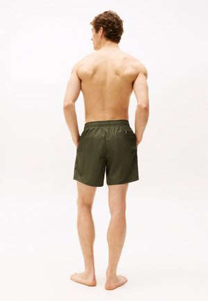 Bañador masculino verde oliva con cintura elástica, detalles cosidos y un único bolsillo trasero. Tela suave y ligera, con una longitud por encima de la rodilla.