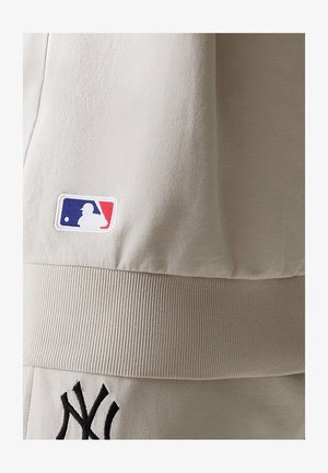 Lichtbeige MLB-kleding met een textuurstof, geribbelde tailleband en geborduurd logo met een zwarte rand en rode en blauwe accenten.