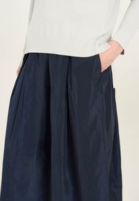Falda plisada azul marino con un acabado texturizado, acompañada de un suéter de rayas gris claro. La falda cuenta con bolsillos laterales.