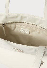 Valge suletav sangaga õlakott, mis on valmistatud siledast materjalist, sisaldab tõmblukuga sisetaskut, kangast voodrit ja sees väikest logomärki.