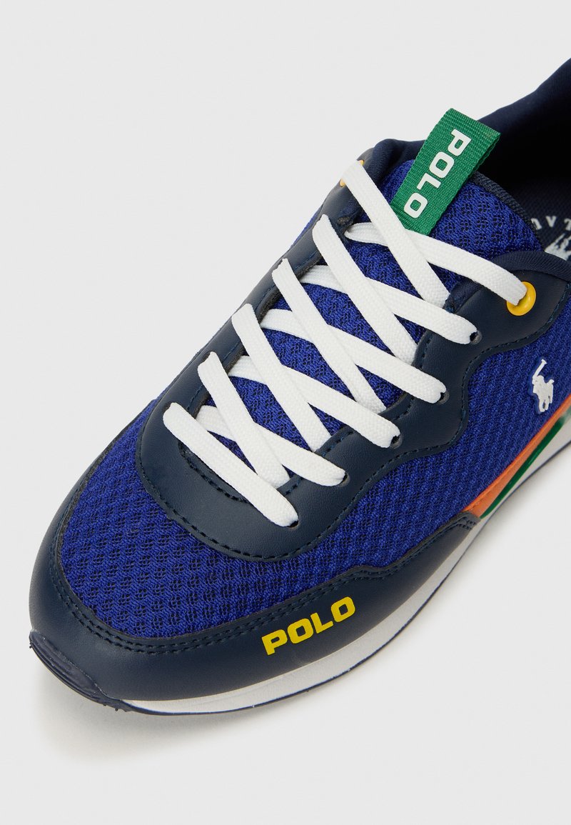 Baskets en maille bleue avec des lacets blancs, accents en cuir marine, étiquette verte "POLO", marquage jaune et détail rayé multicolore sur la semelle.