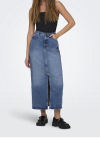 Denim maxikjol i medelblått, med en framtill slit och klassiska fickor. Kombinerad med en svart ärmlös topp och kraftiga svarta skor.