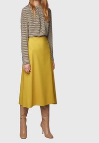 Blouse à motifs noir et blanc associée à une jupe évasée jaune. Des bottes beiges montantes complètent la tenue.