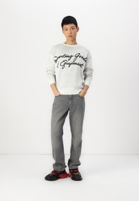 Gray sweater with black script text, gray jeans, and black sneakers with red accents. Simple design, soft texture, relaxed fit.