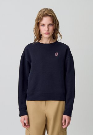 Sweat-shirt noir en coton avec des poignets et un ourlet côtelés, arborant un petit logo rouge sur la poitrine. Texture douce et coupe décontractée.