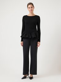 Sort langærmet top med peplumkant, tekstureret stof, kombineret med sorte bukser med vide ben og blanke sorte hæle. Enkel rund halsudskæring.