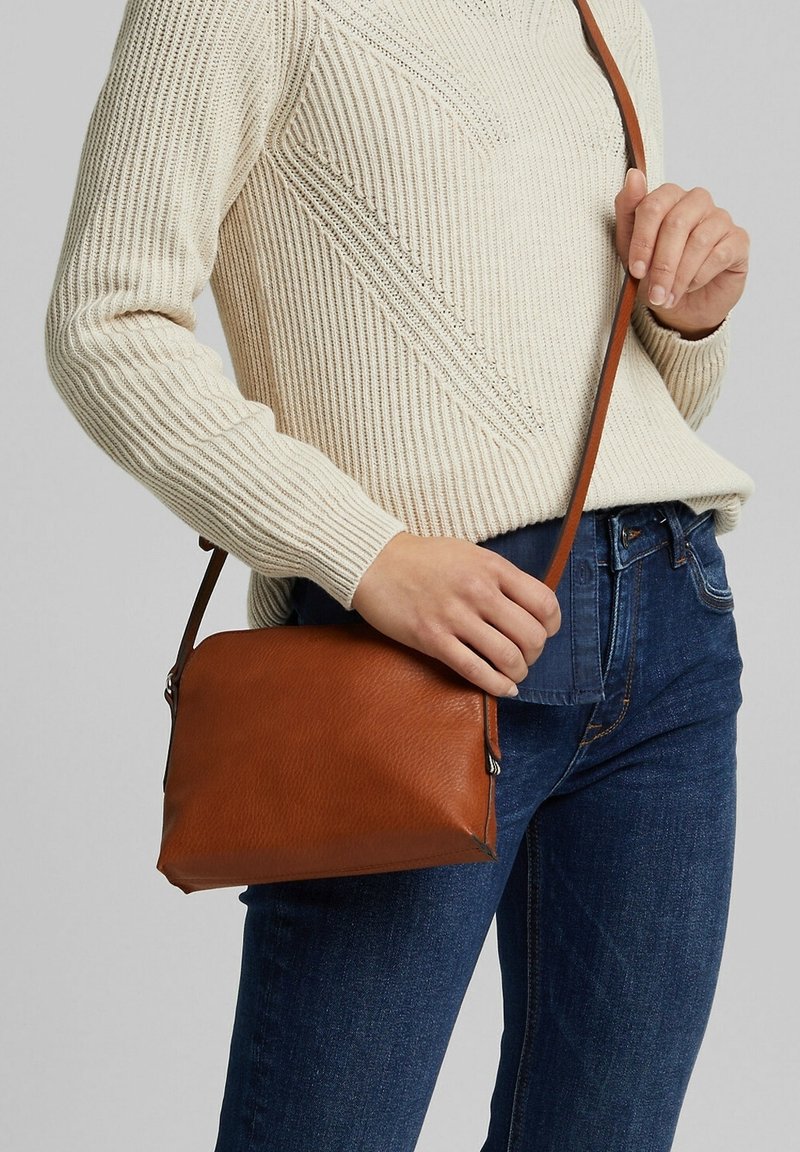 Sac bandoulière en cuir marron avec une texture lisse, de forme rectangulaire et une bandoulière réglable. Simples éléments de quincaillerie visibles.
