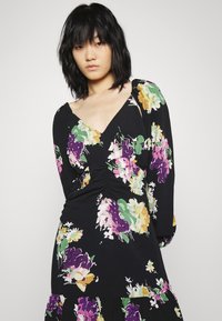 Vestido preto com flores vibrantes em tons de roxo, rosa e amarelo, decote em v, mangas longas e detalhe de cintura franzida.