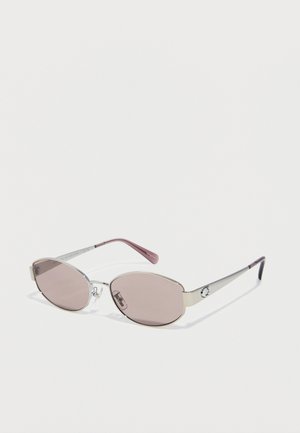Oval sunglasses with thin silver metal frames and brown tinted lenses, resting on a white surface.
