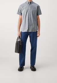 Grå kortärmad skjorta med knappar, blå lösa jeans och svart handväska med korta handtag. Skor är svarta, kraftiga kängor.