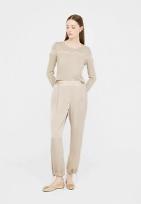 Maglione beige lavorato a maglia con un motivo sulle spalle, abbinato a pantaloni beige tapered con coulisse. Il look è completato da ballerine oro.