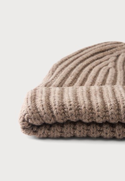 Bonnet beige en maille côtelée plié avec un revers, présenté sur un fond clair uni.