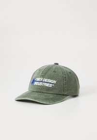 Green cotton cap with embroidered "Obey Design Industries" in white and blue. Features a curved brim and adjustable strap at the back.