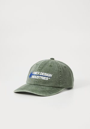 Gorra de algodón verde con el bordado "Obey Design Industries" en blanco y azul. Cuenta con un ala curva y una correa ajustable en la parte trasera.