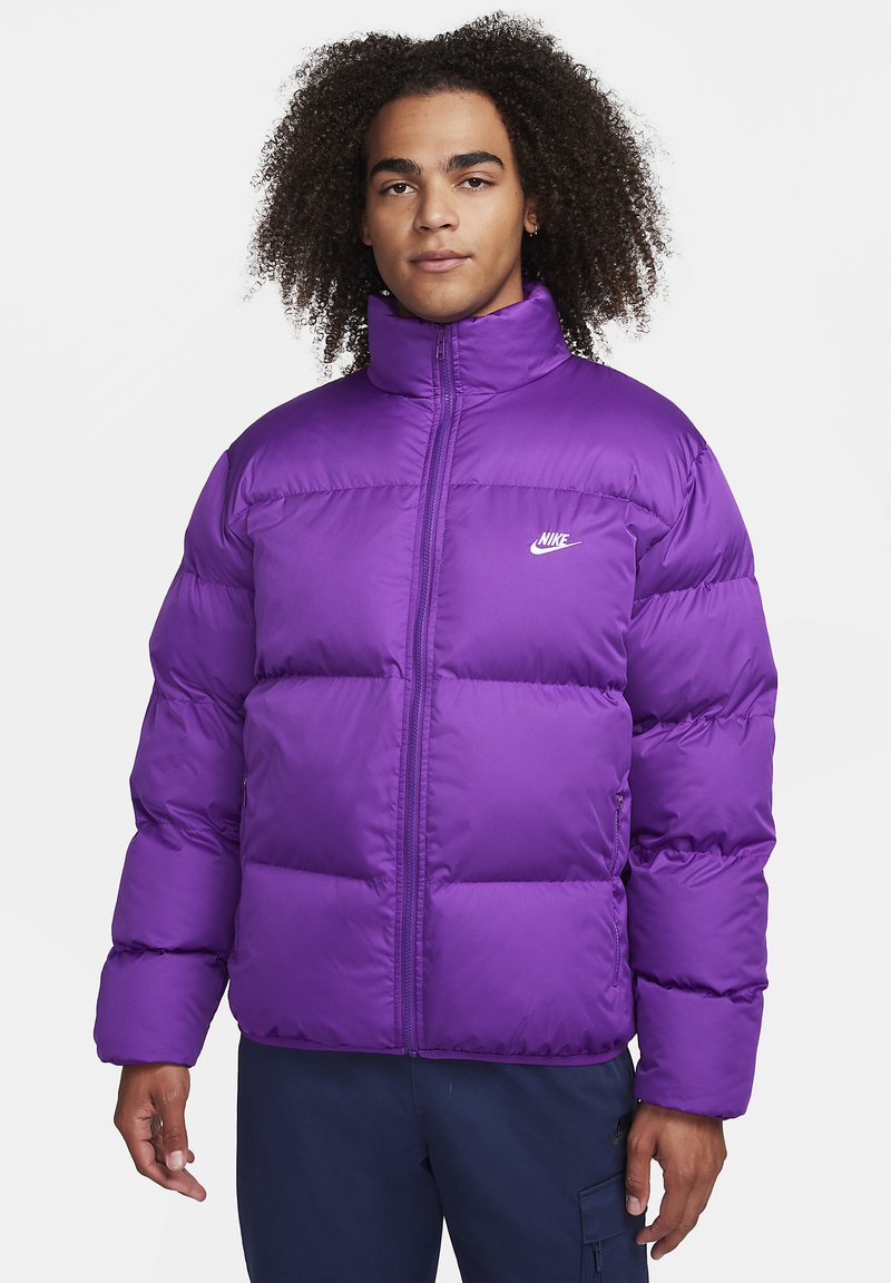 Giacchetto imbottito viola con colletto alto, chiusura con zip e logo Nike bianco. Il materiale è liscio e morbido, con sezioni trapuntate equidistanti.