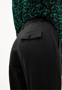 Černé kalhoty na míru s rovnými nohavicemi, hladkou texturou a jednou zadní kapsou se zapínáním na knoflík.