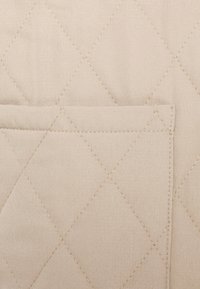 Tissu matelassé beige avec un motif de coutures en losange et une poche rectangulaire cousue sur la surface.
