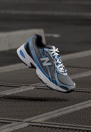 Grå løpesko med mesh-overdel, blå detaljer og hvite lisser. Har en polstret såle og teksturert grep under.