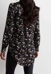 Musta pitkähihaisten paita, jossa on kuvioitu muotoilu valkoisilla ja beigen pisteillä, suora helma ja rento istuvuus. Pehmeä kangastuntuma.