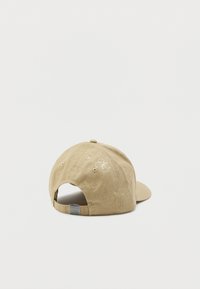 Casquette en coton beige avec un bord courbé, présentant des motifs de logo en relief et une sangle réglable à l'arrière. Le tissu texturé est visible.