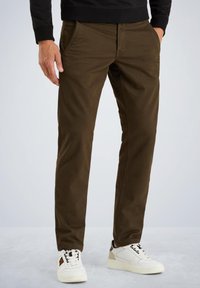 Brune afslappede bukser lavet af et tykt stof, med sidelommer og en slim fit design. Båret med hvide sneakers.