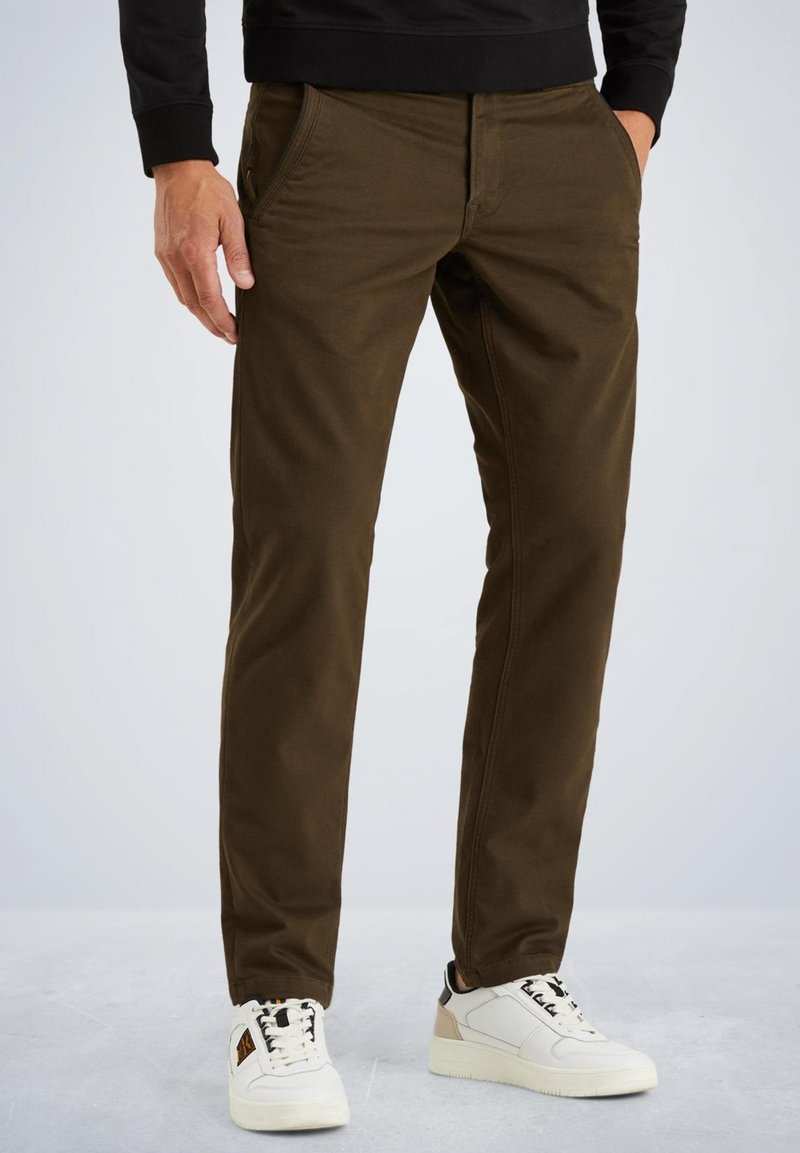 Brune afslappede bukser lavet af et tykt stof, med sidelommer og en slim fit design. Båret med hvide sneakers.