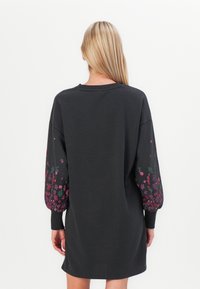 Svart hettekjole med lange ermer, prydet med fargerik blomsterbroderi på ermerne og en avslappet passform. Myk, teksturert stoff.